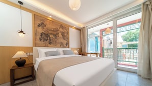 A hotel room with a bed, bedside lamps, a large painting on the wall, and a balcony with a view. - Forbidden City Hutong Courtyard (Beijing)