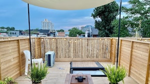 A rooftop patio with a wooden deck, a table with a tray, two potted plants, and a large air conditioning unit. - Forbidden City Hutong Courtyard (Beijing)
