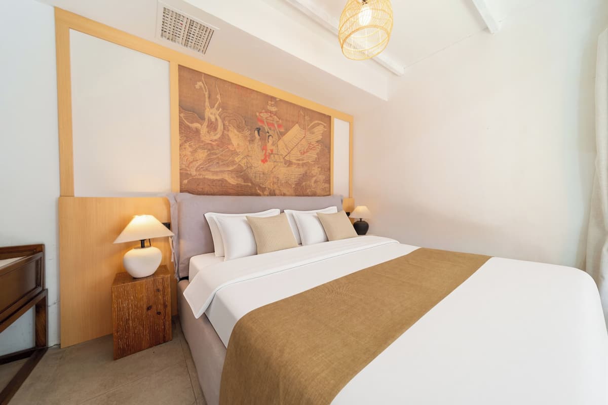 A bedroom with a large bed, two bedside tables with lamps, a wooden headboard, and a large painting on the wall.