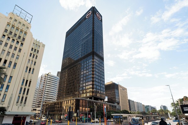 A modern high-rise building with a glass facade and a prominent logo at the top.
