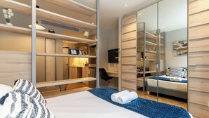 A modern hotel room with a large bed, a desk, and a wardrobe with a mirror.