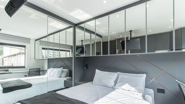 Ein modernes Hotelzimmer mit einem großen Bett, einem Einzelbett, einem Schreibtisch und einer großen Spiegelwand.