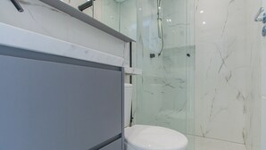 Ein modernes Badezimmer mit Duschkabine aus Glas, einer weißen Toilette und einer Marmor-Spritzschutzwand.