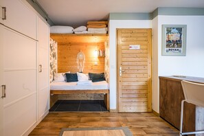 A compact room with a bunk bed, wooden walls, a desk, and a chair.