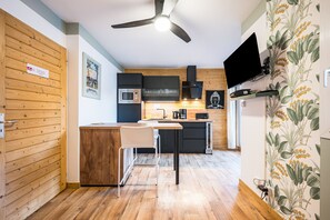 A modern kitchen with wooden cabinetry, a built-in microwave, and a flat-screen TV mounted on the wall.