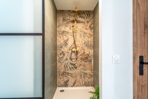 A shower with a gold showerhead, a marble-patterned wall, and a wooden door.
