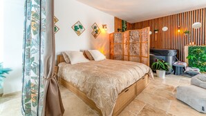 Ein Schlafzimmer mit einem Bett, einem Holzkopfbrett, einem Wandregal, einem kleinen Tisch und einer Topfpflanze.