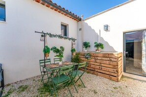 Un patio con una mesa y sillas, plantas en macetas y un banco de madera.