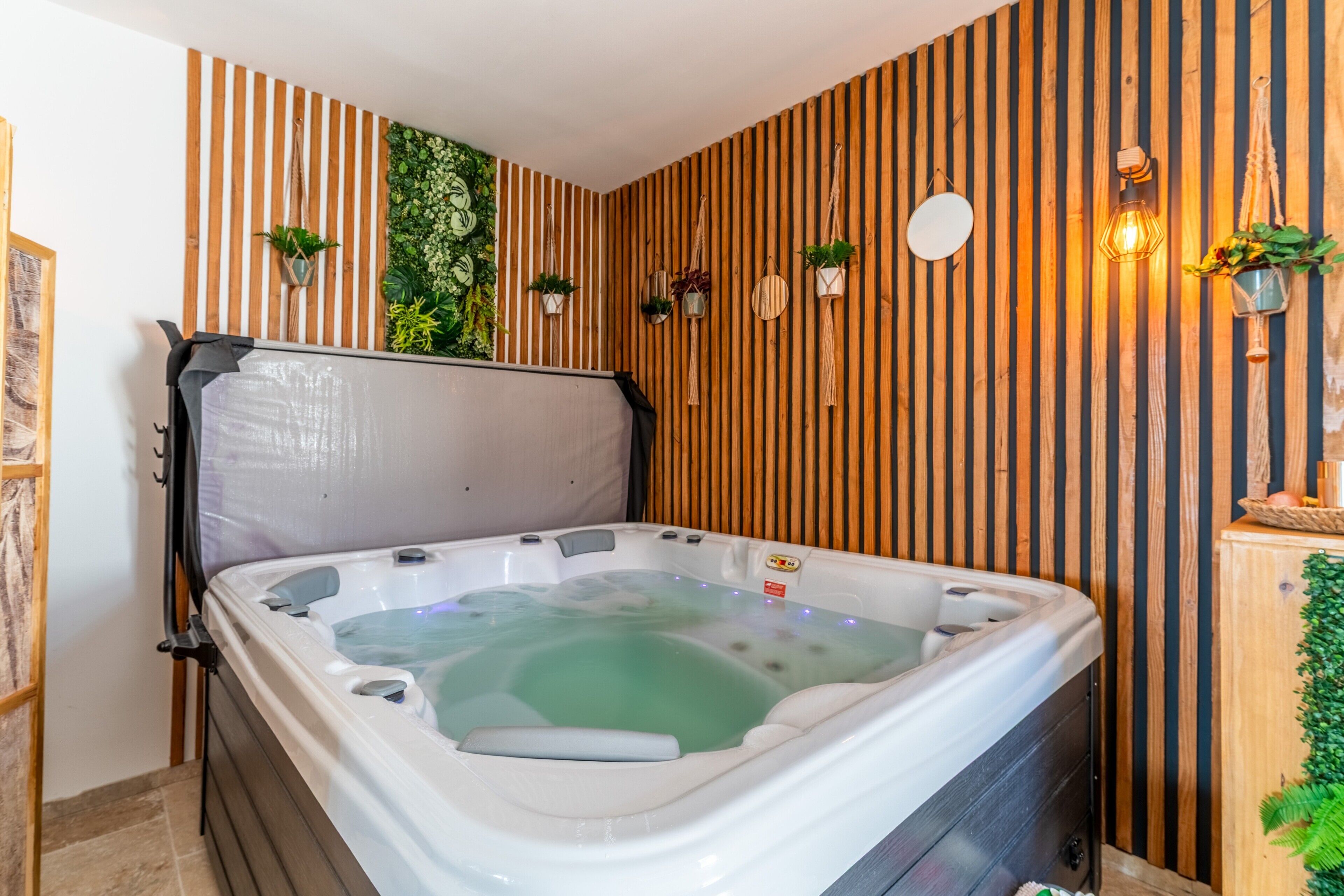 Banyera d'hidromassatge en una habitació amb revestiment de fusta, plantes en testos i llums penjades a la paret.
