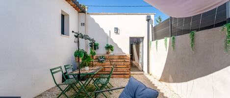 A patio with a table and chairs, a wooden bench, and potted plants.