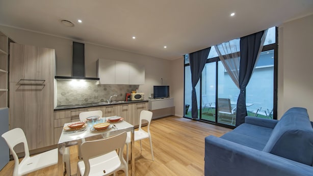 A modern kitchen with white cabinets, a dining table with chairs, a blue sofa, and large windows with curtains. - Sun & moon house (Cagliari)