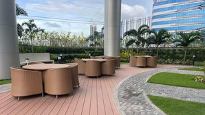 An outdoor seating area with wicker furniture, a paved deck, and a landscaped garden with grass and plants.