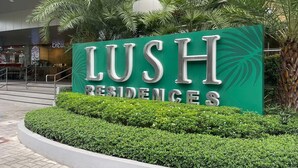 A sign for LUSH Residences with a modern design, surrounded by well-maintained greenery and a staircase leading to an entrance.