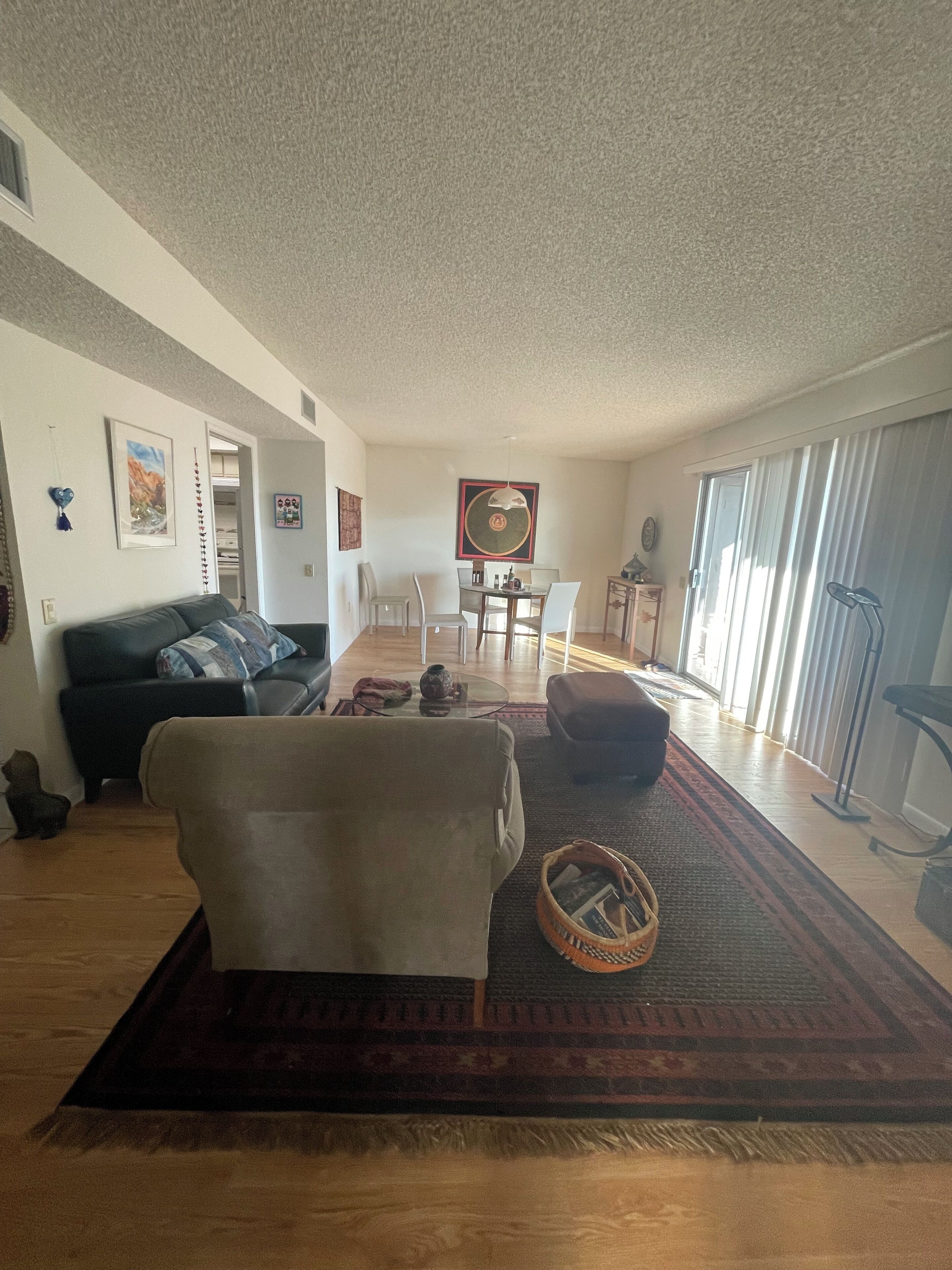 Un salón con sofá, una mesa de centro y una mesa de comedor con sillas. Hay una ventana con cortinas y una puerta que da a otra habitación.