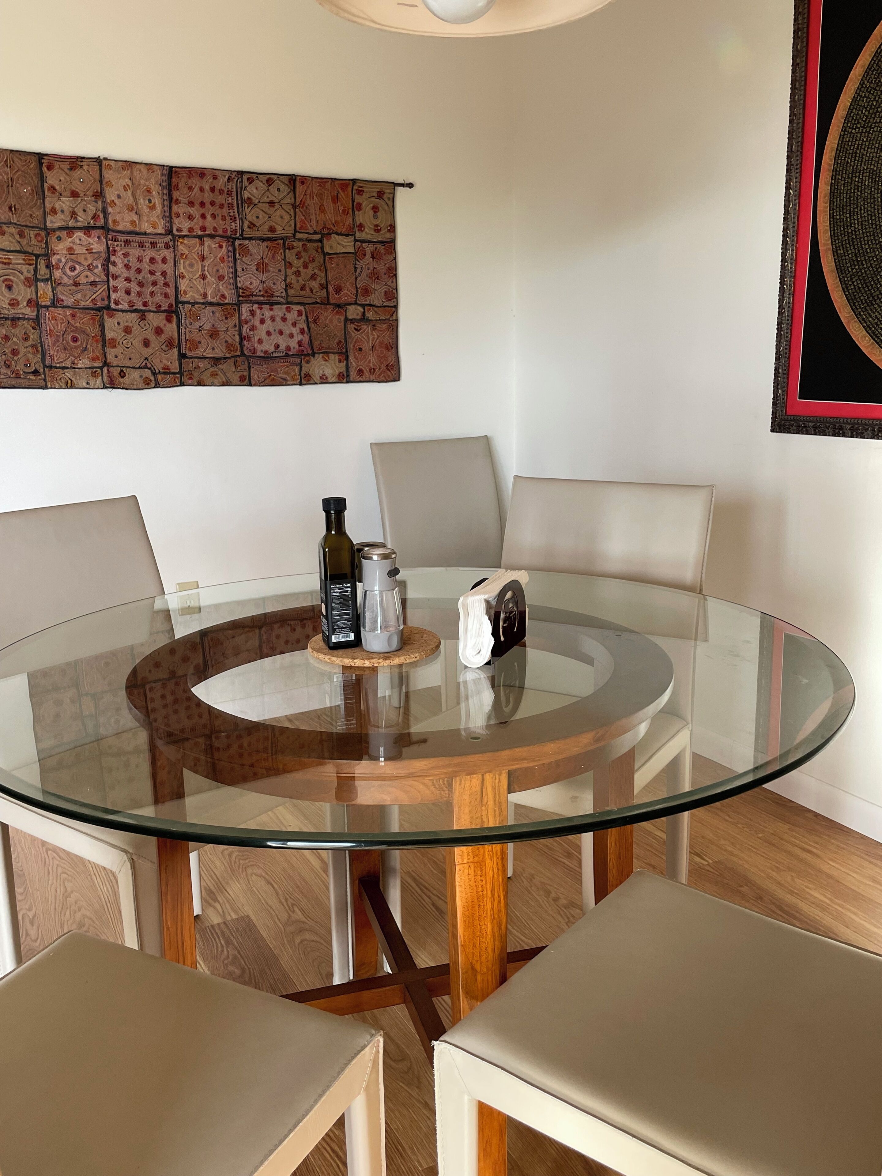 Una mesa redonda de vidrio con un posavasos de corcho, una botella y una cafetera.