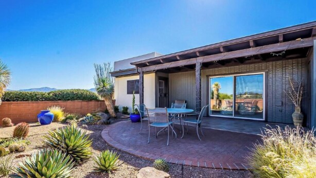 A modern house with a patio, a dining area, and a large sliding glass door leading to a backyard.