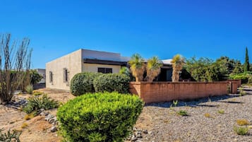 Un edificio moderno con techo plano, rodeado de un jardín ajardinado con arbustos variados y algunas palmeras.