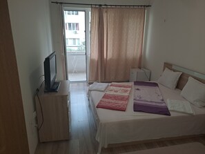 A bedroom with a bed, a TV, a desk, and a window with curtains. - My cosy place (Burgas)
