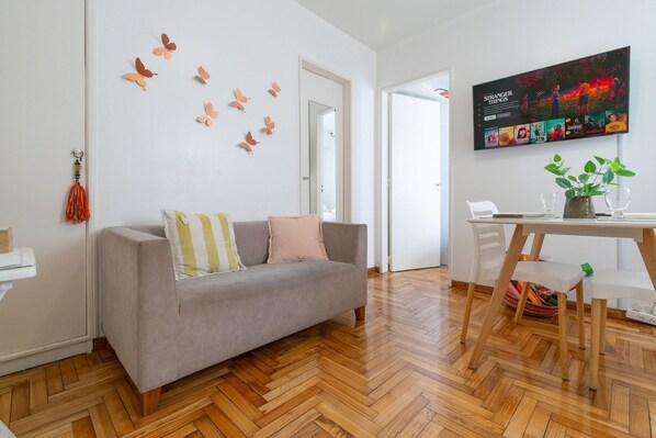 Un salon moderne avec un canapé gris, un parquet en bois disposé en chevrons, un téléviseur fixé au mur et des autocollants décoratifs représentant des papillons.