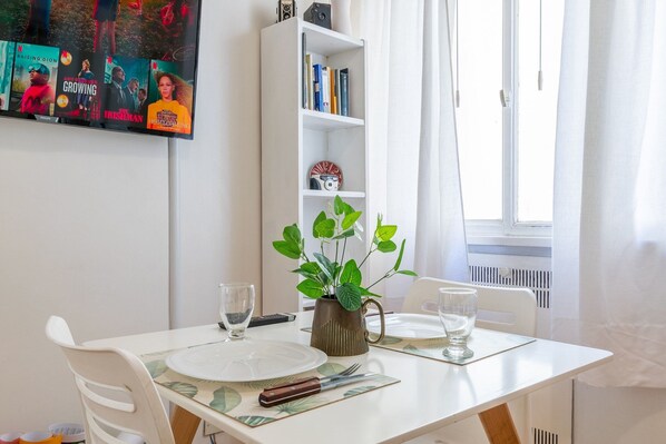 A dining area with a table set for two, a bookshelf, and a TV displaying movie posters.