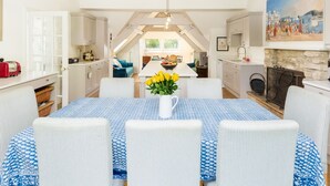 Een moderne keuken met witte kastjes, een eethoek met blauw-wit geruite tafelkleden en een schilderij aan de muur.