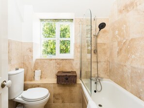 Ein Badezimmer mit Toilette, Bidet, einer Duschkabine, einem Fenster mit Blick auf Bäume und einem Korbwägelchen auf dem Boden.