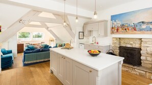 Een ruime woonkamer met een groot kookeiland, een keuken met witte kastjes en een stenen open haard.