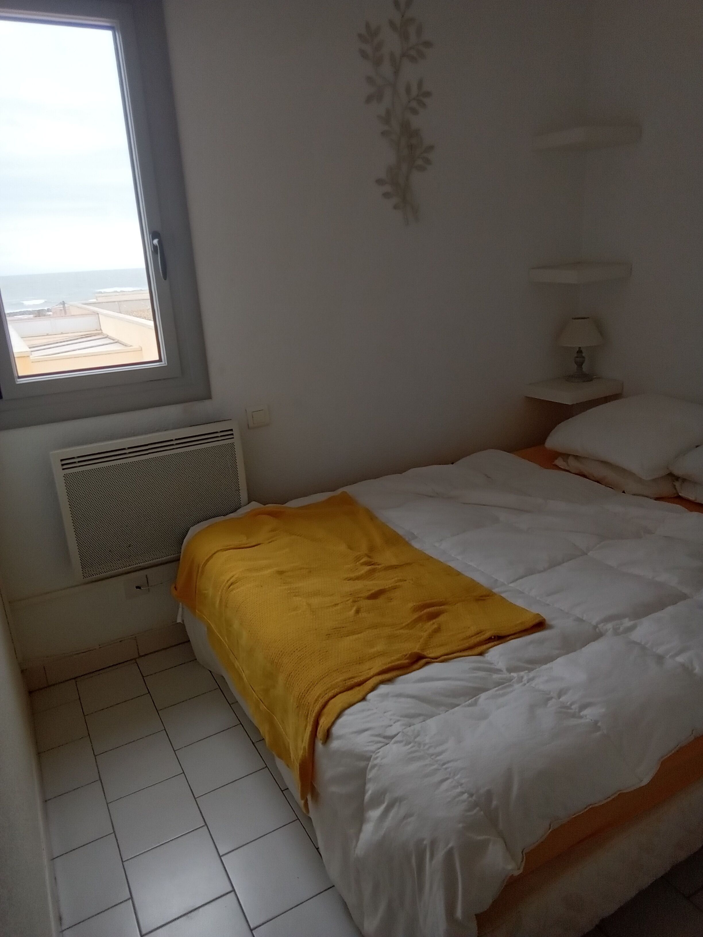 A bedroom with a bed, a window, a wall-mounted lamp, and a radiator.