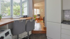 A modern kitchen with a built-in washing machine, a dining area with a table and chairs, and large windows with blinds.