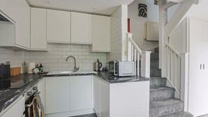 A modern kitchen with white cabinetry, a granite countertop, and a microwave. There is a staircase leading to a landing with a view of the outside.