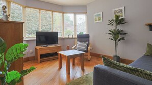 A living room with a TV, wooden furniture, a sofa, and large windows.