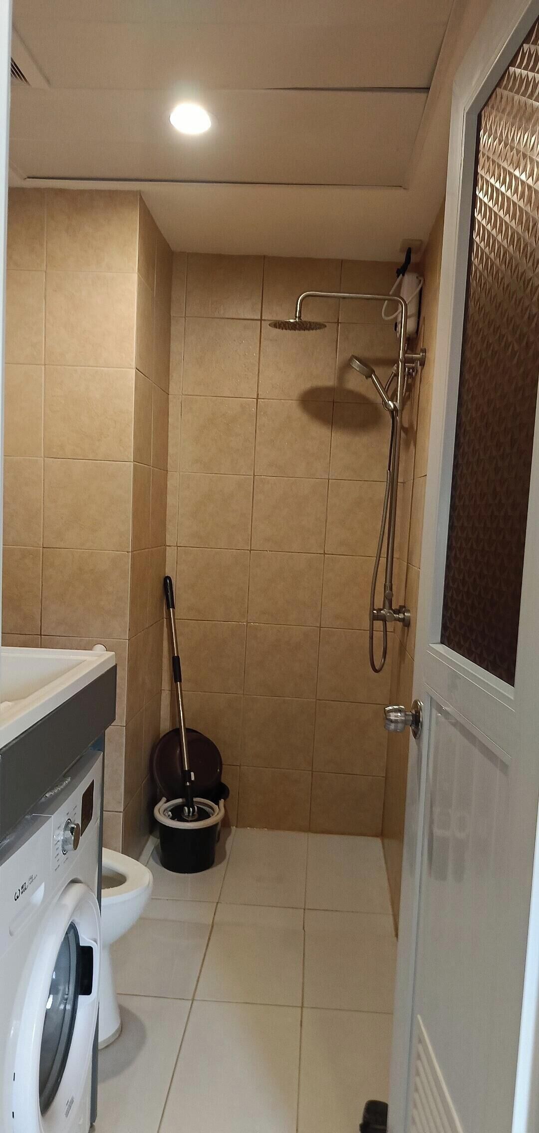 Un baño con baldosas color beige, ducha, inodoro y lavadora.
