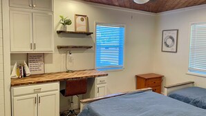 Une chambre avec un plafond en bois, un bureau avec une chaise, deux lits et une fenêtre avec des stores.