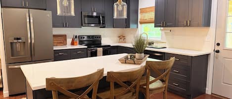 Una cocina moderna con armarios oscuros, electrodomésticos de acero inoxidable y una isla central con sillas.