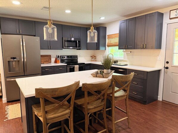 A modern kitchen with dark cabinets, stainless appliances, and a central island with chairs. - Peaceful home across from River, 24x24 garage (Palatka)