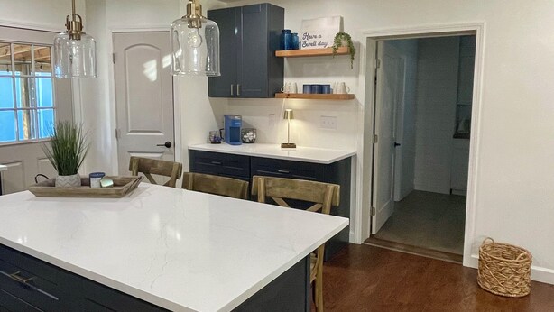 Une cuisine moderne dotée d’un grand îlot central, de meubles de rangement aux couleurs sombres et d’un plan de travail lumineux.
