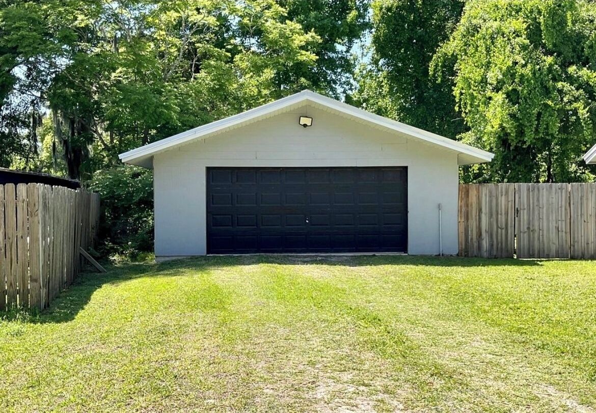 A single-story garage with a dark garage door, surrounded by a wooden fence, and a grassy yard.