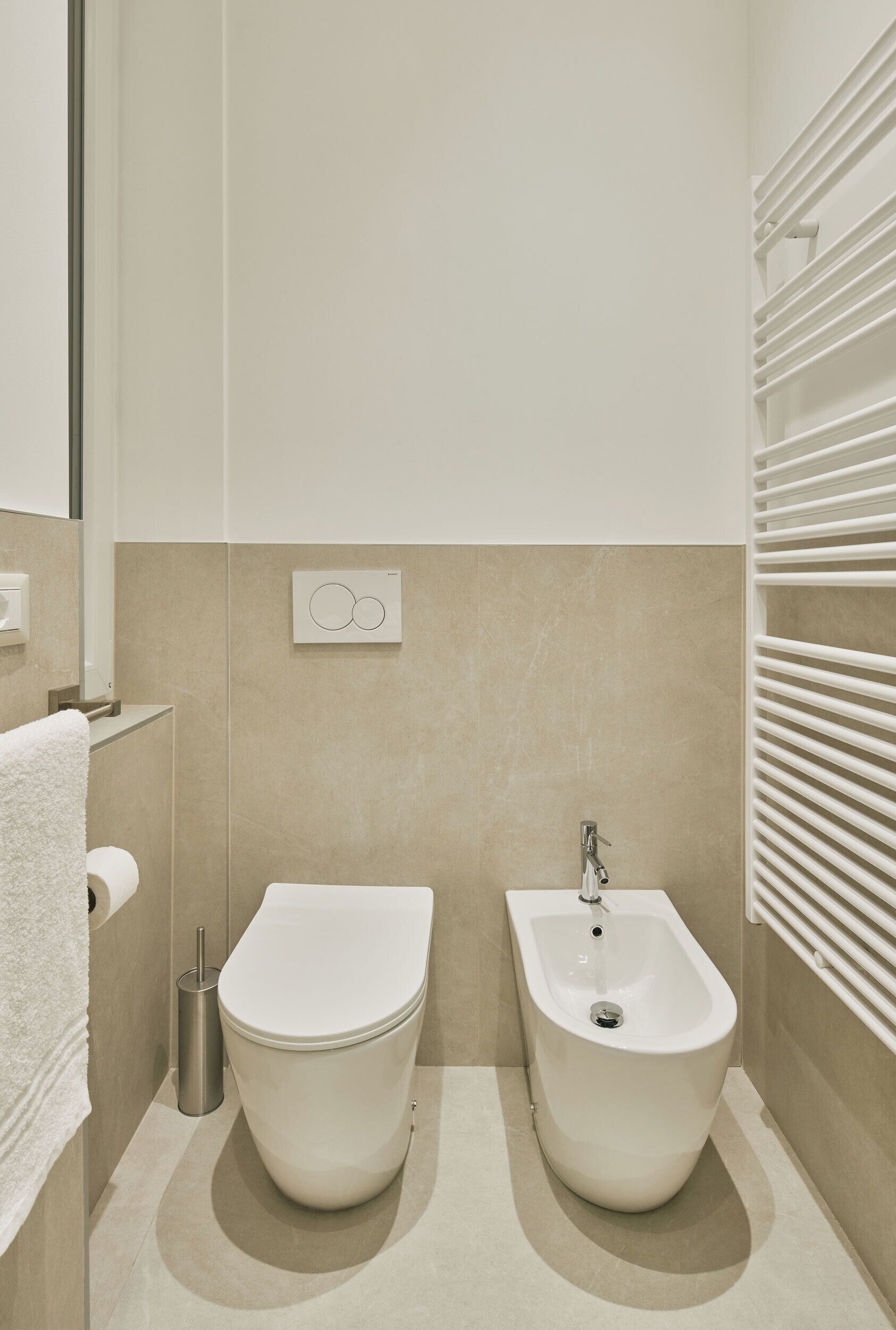 A modern bathroom with a toilet, bidet, and a towel rack.