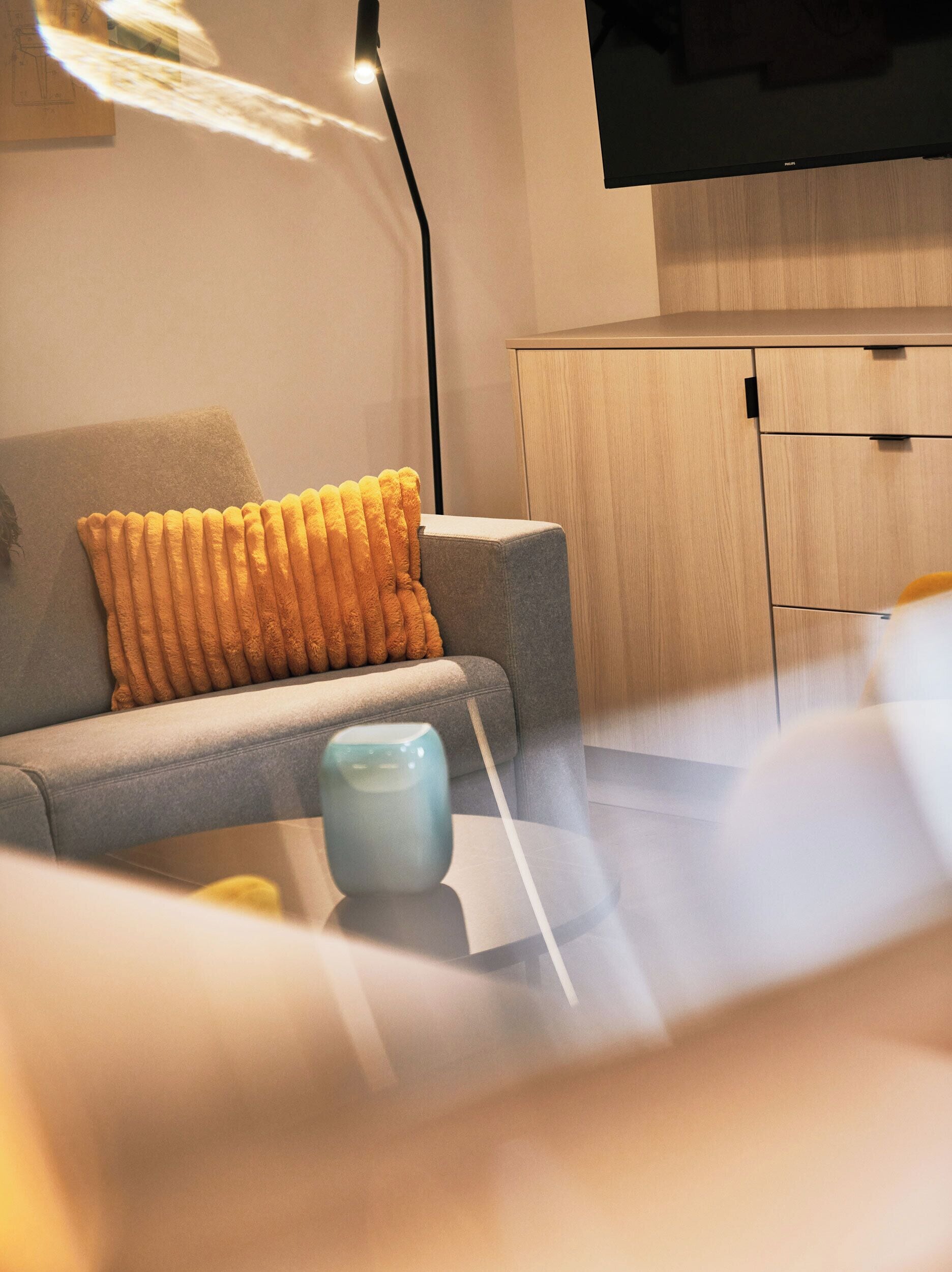 Ein modernes Wohnzimmer mit einem grauen Sofa, einer blauen Vase und einem Holzkabinett.