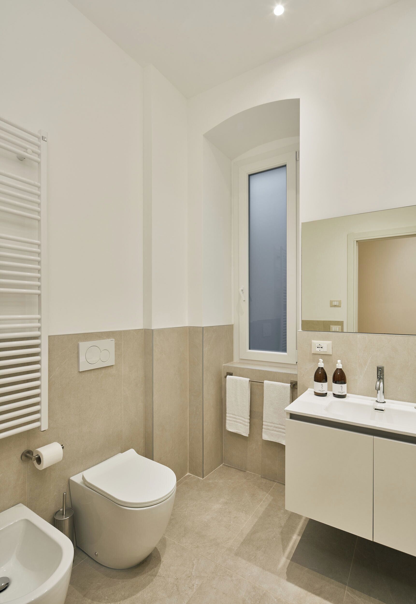 A modern bathroom with a toilet, bidet, sink, and mirror.