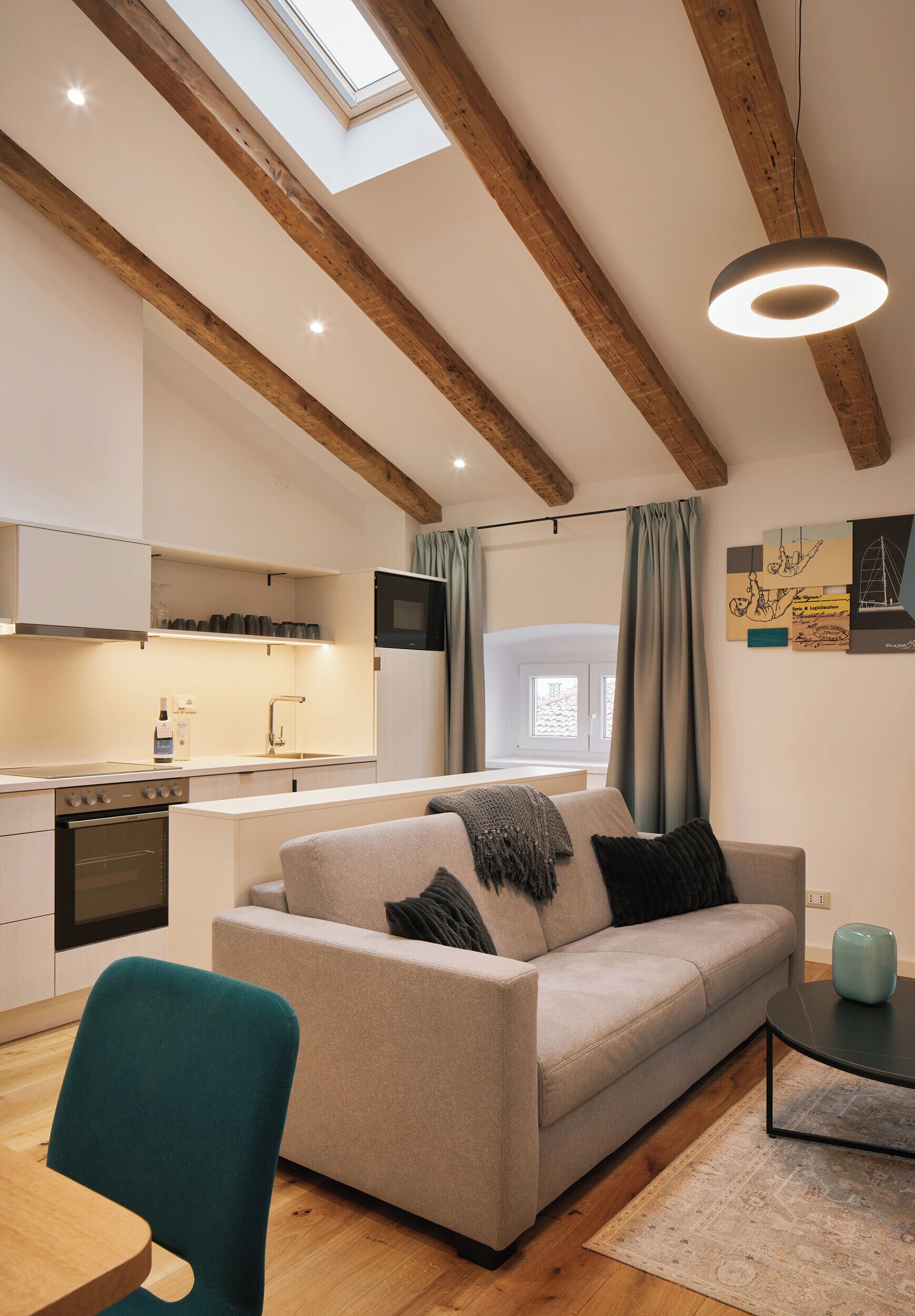 A modern kitchen with wooden beams, a dining area with a teal chair, and a living room with a sofa and a coffee table.