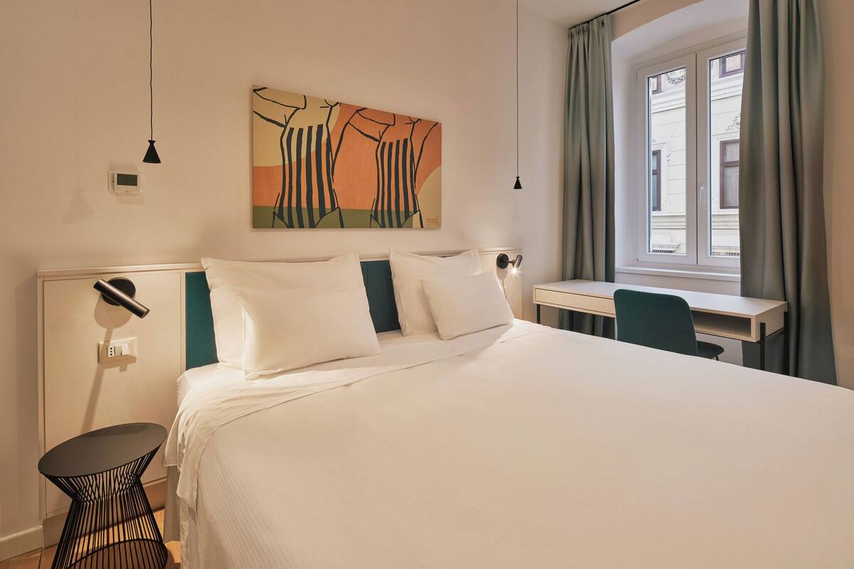 Ein ordentlich eingerichtetes Hotelzimmer mit einem großen Bett, einem Schreibtisch und einem Bild an der Wand.