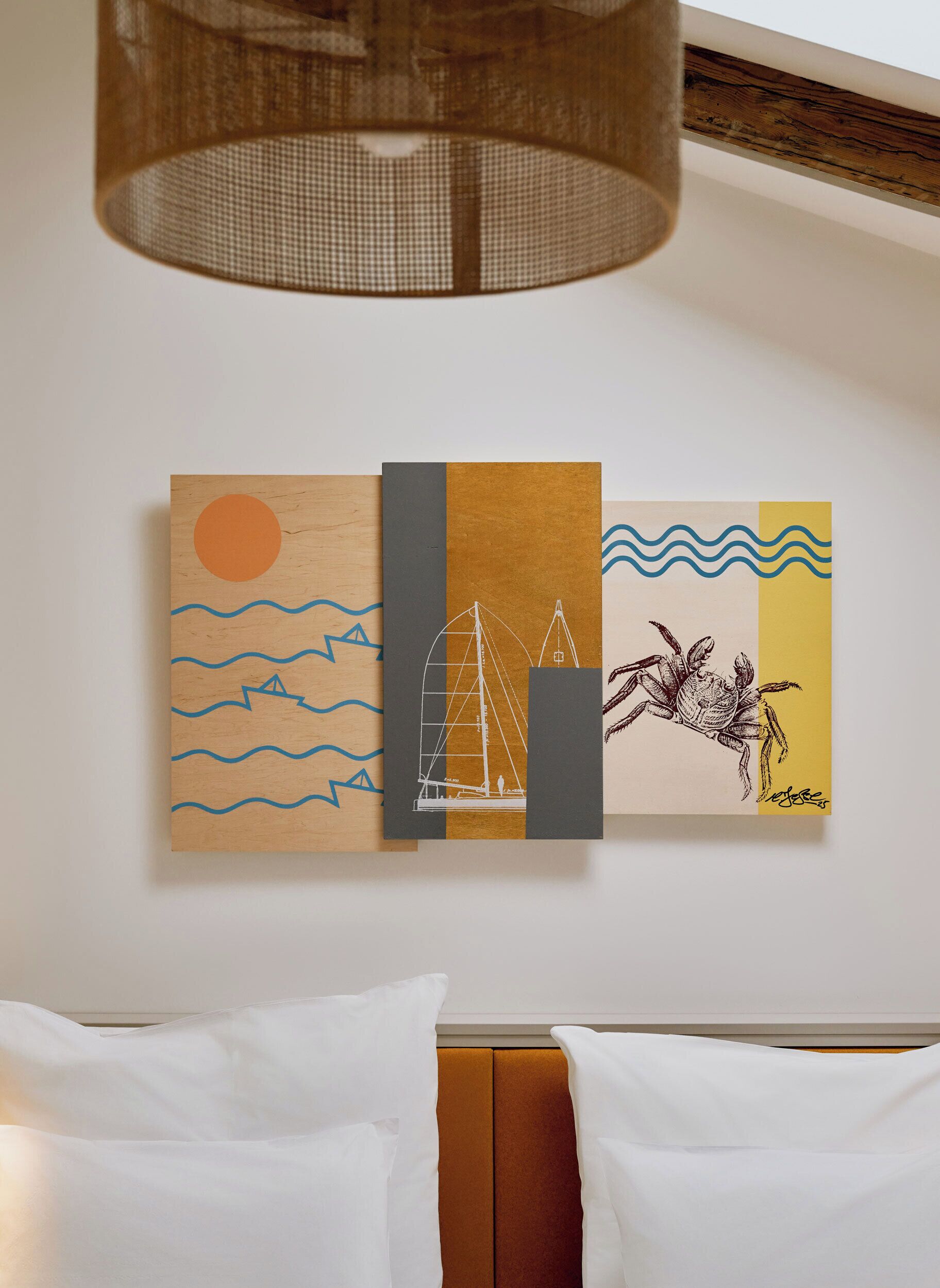 A wall with three artworks depicting a sun, waves, and a sailboat.