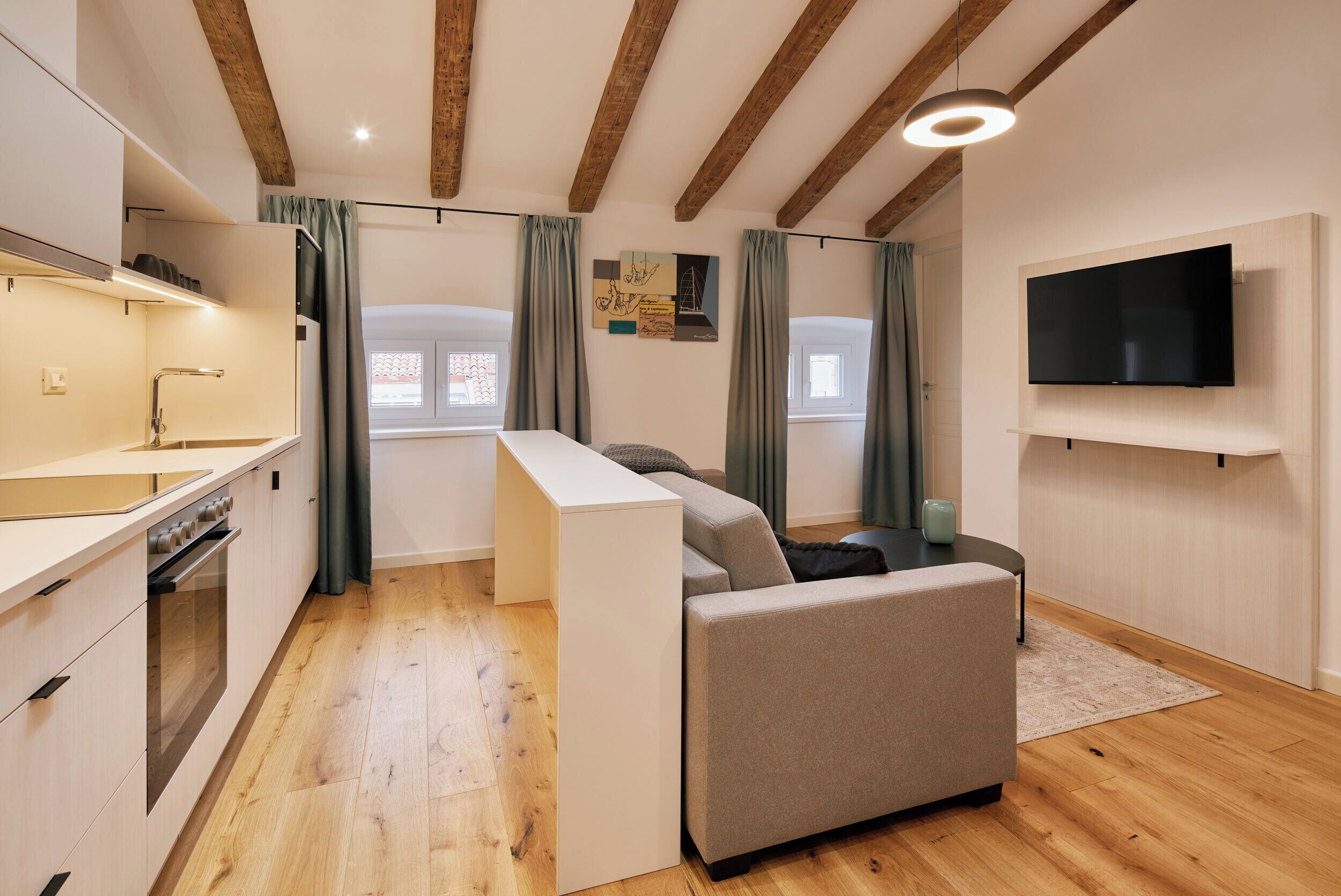 A modern kitchen with wooden beams, a built-in oven, and a flat-screen TV mounted on the wall.
