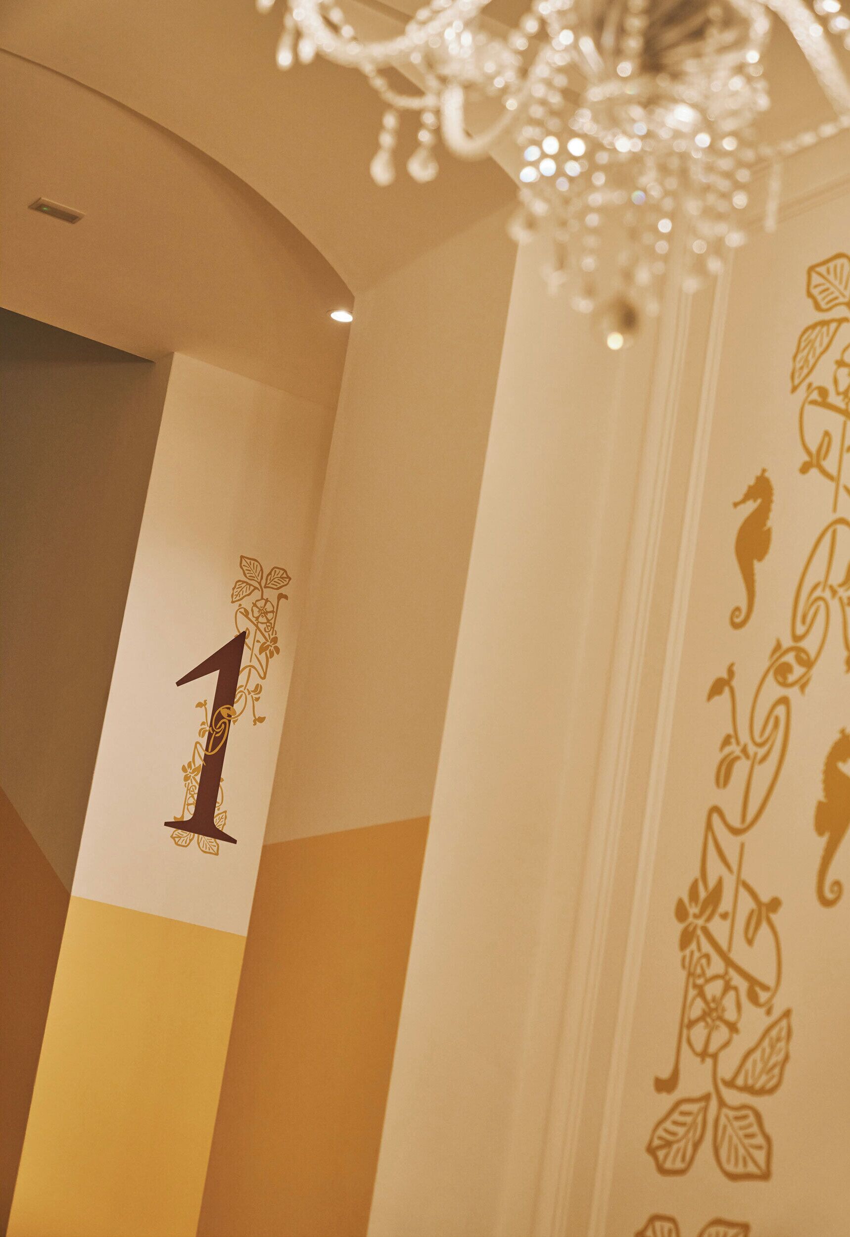 A hallway with a number '1' on the wall, a chandelier, and floral wall decorations.