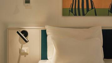 A neatly made bed with white linens, a bedside lamp, a power outlet, and a painting on the wall.
