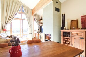 Una habitación acogedora con una mesa de comedor de madera, una taza roja con una planta, un sofá y una zona de cocina con armarios de madera y un televisor.