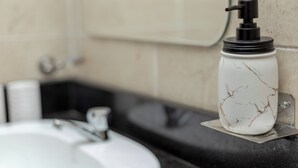 Ein Badezimmer mit einem weißen Marmorwaschbecken, einer schwarzen Arbeitsplatte und einem an der Wand befestigten Seifenspender.