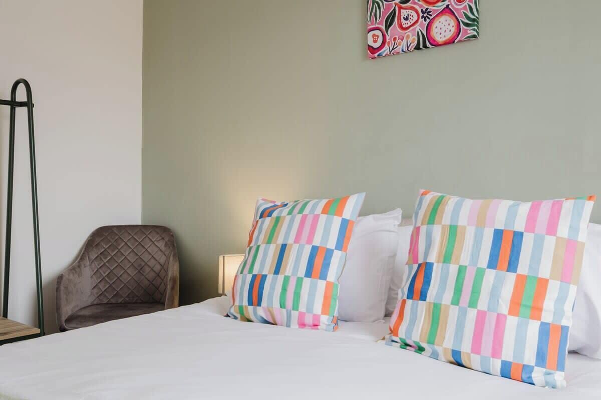 Una habitación de hotel con una cama, dos almohadas de estampado a rayas, una silla y una obra de arte en la pared.