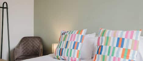 Una habitación de hotel con una cama, dos almohadas de estampado a rayas, una silla y una obra de arte en la pared.